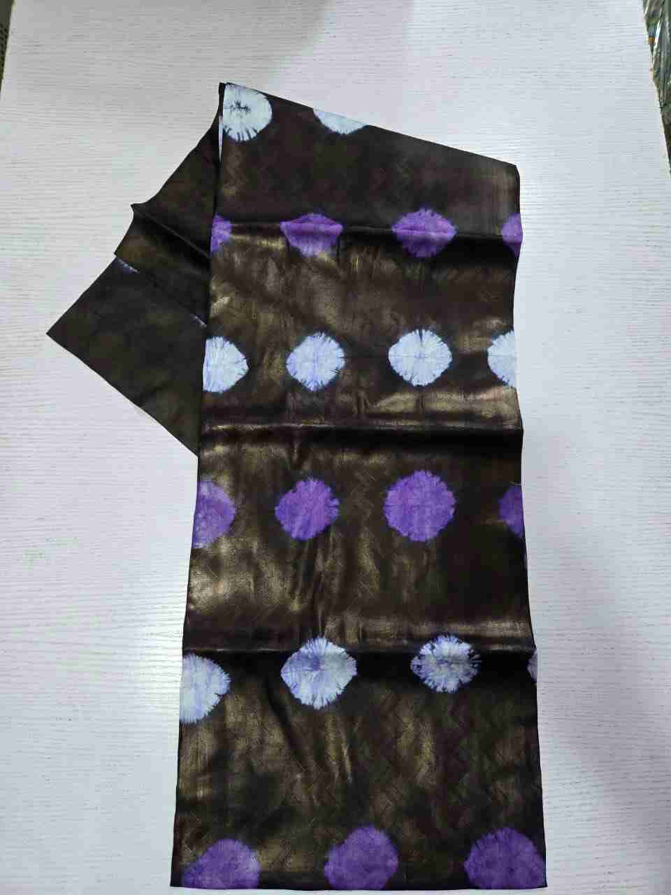 Richly toned Adire Kampala fabric featuring rows of deep amethyst-purple and white tie-dye burst motifs on a metallic bronze base with chevron-textured undertones