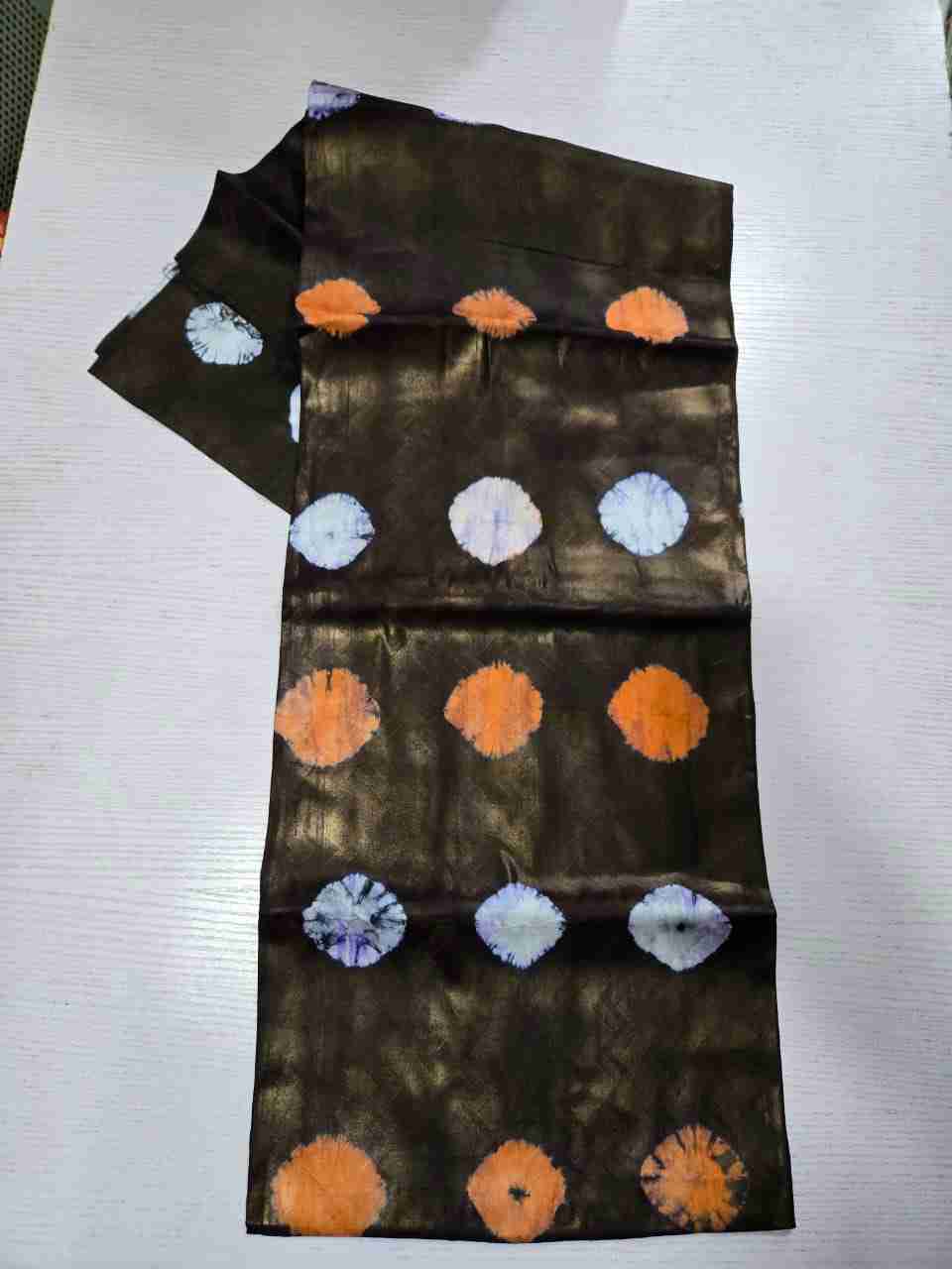 Traditional Adire tie-dye Kampala fabric featuring rows of vibrant orange and contrasting icy-white spiral burst motifs across a metallic bronze-over-black base